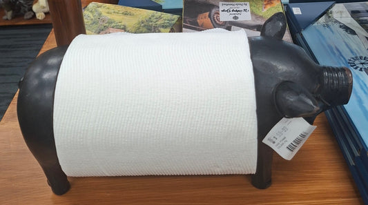 Black cow-shaped paper towel holder with a roll of paper towels on a wooden shelf.