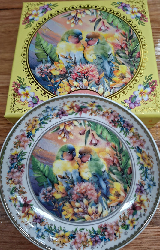 Decorative plate with floral and bird design next to its packaging on a wooden surface