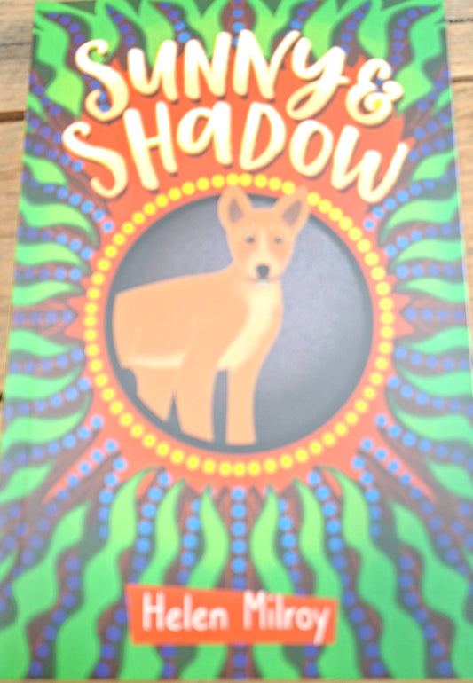 Book cover of 'Shadows' by Helen Milroy with colorful design on a wooden surface